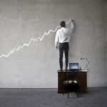 business person standing on desk drawing a line on a wall